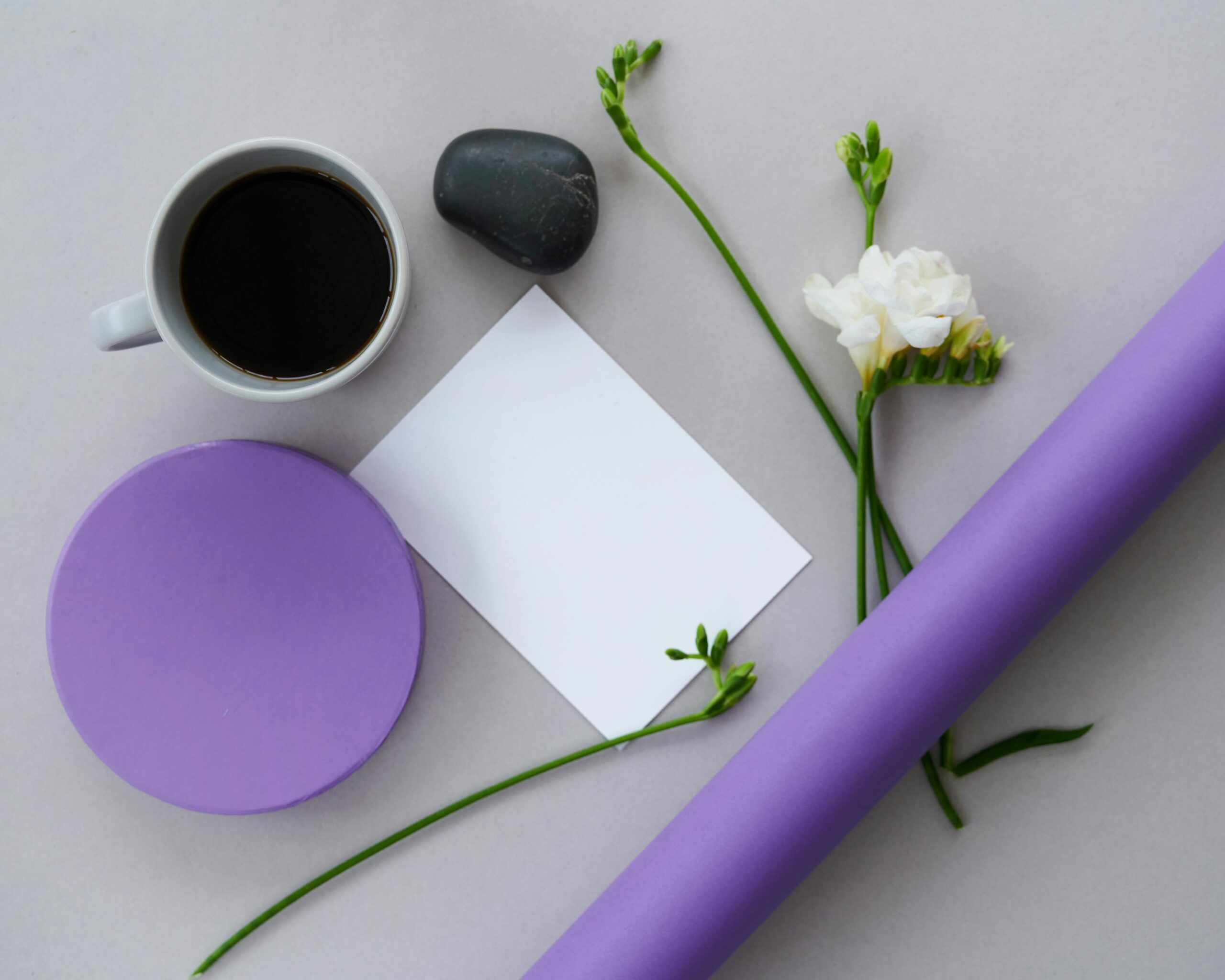 Aesthetic flat lay featuring coffee, white flowers, a note, and a purple arrangement on a white background.