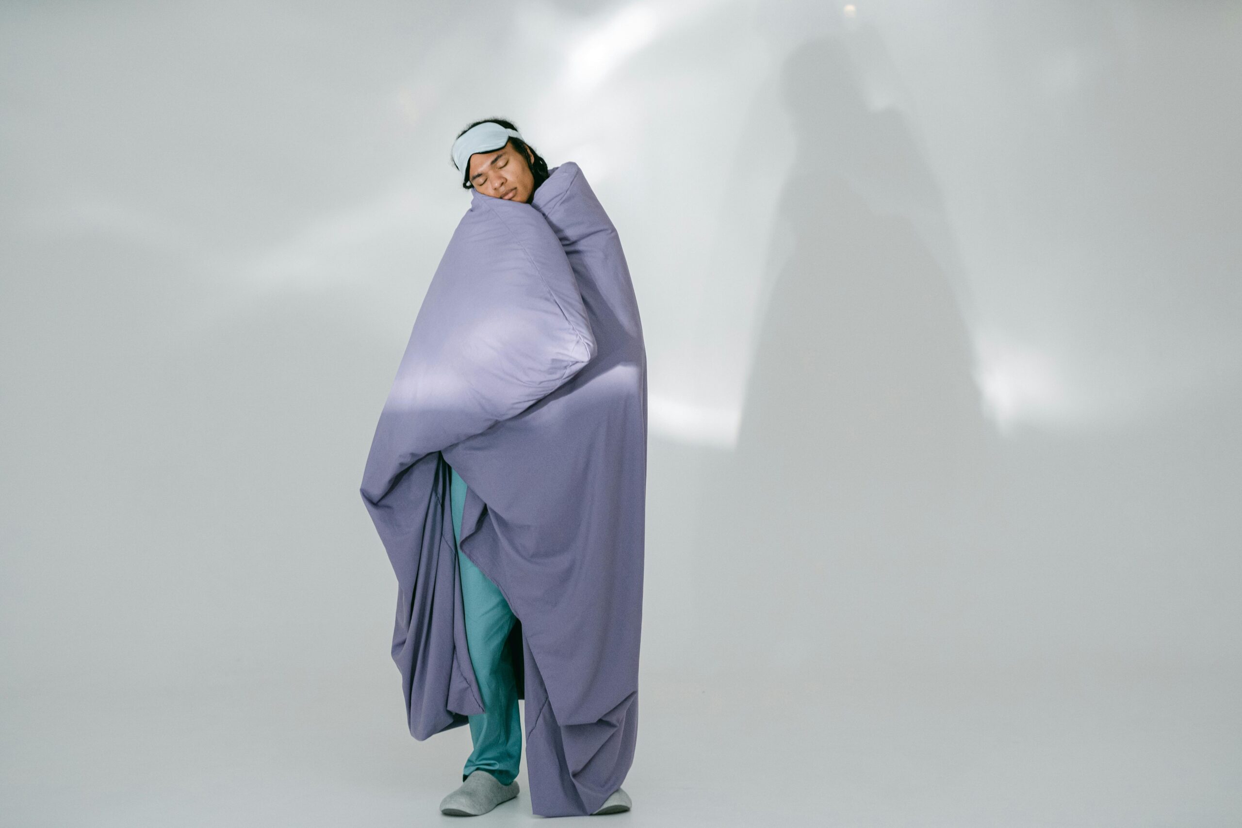 African American man wrapped in a purple blanket, wearing eye mask, resting in studio.